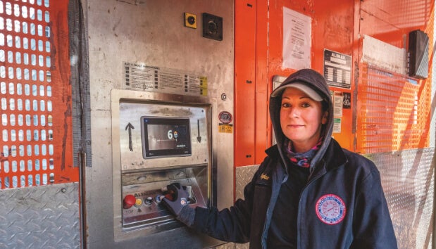 A construction worker operates a control panel on a construction site, focused and determined, with safety gear on.