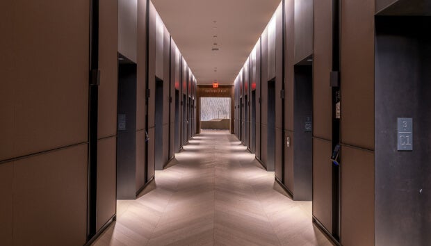 Modern corridor lined with energy-efficient elevators using destination dispatch for improved energy savings.