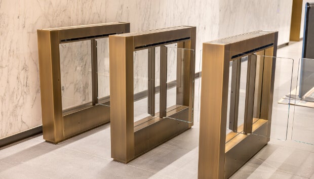 Modern entry gates with glass barriers in a clean, marble-lined building lobby.