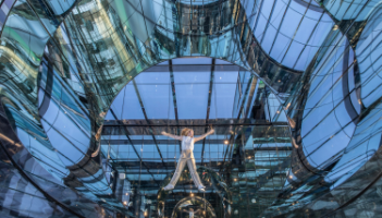 A person lying down in an interactive art exhibit in NYC, surrounded by curved, reflective surfaces.