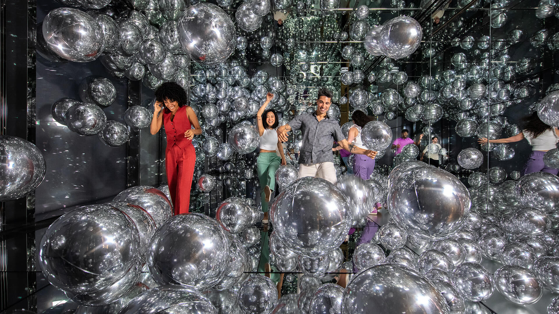Enthusiastic guests playing and laughing in a room full of balloons.