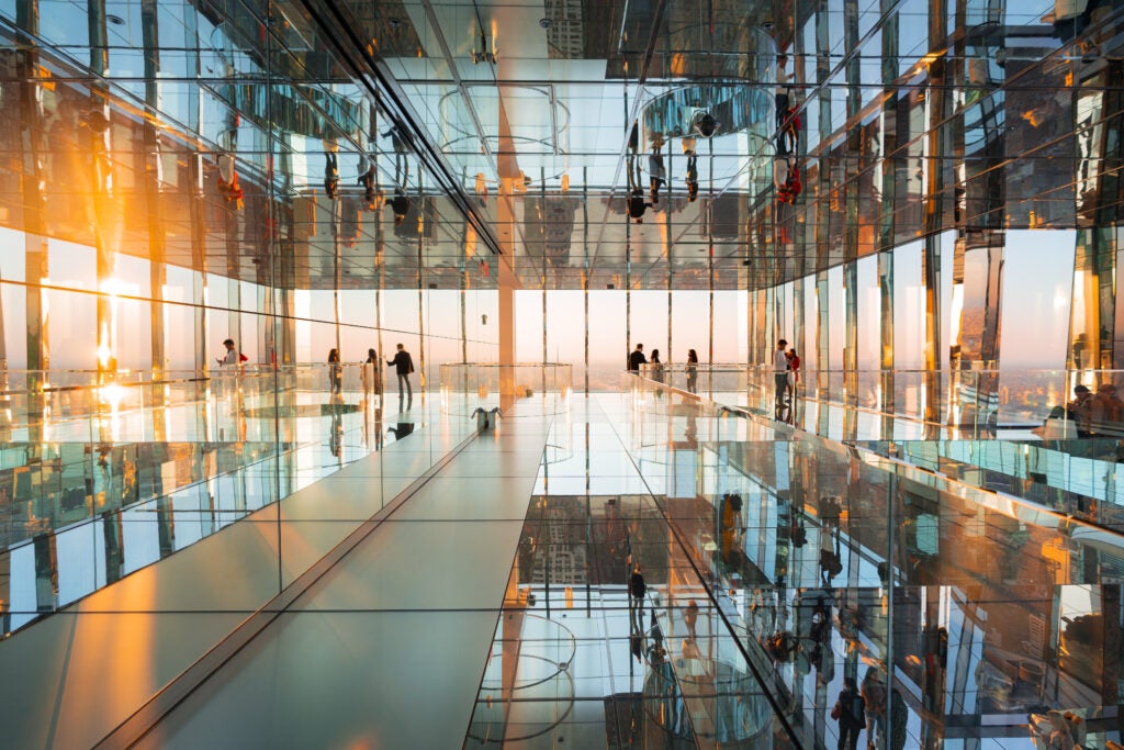 Visitors walking through the mirrored glass observation deck at SUMMIT, reflecting the sunset views of New York City.