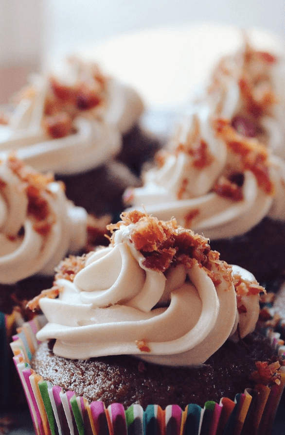 Delicious New York cupcake topped with creamy white frosting and sprinkled with crunchy bits, presented in colorful paper.